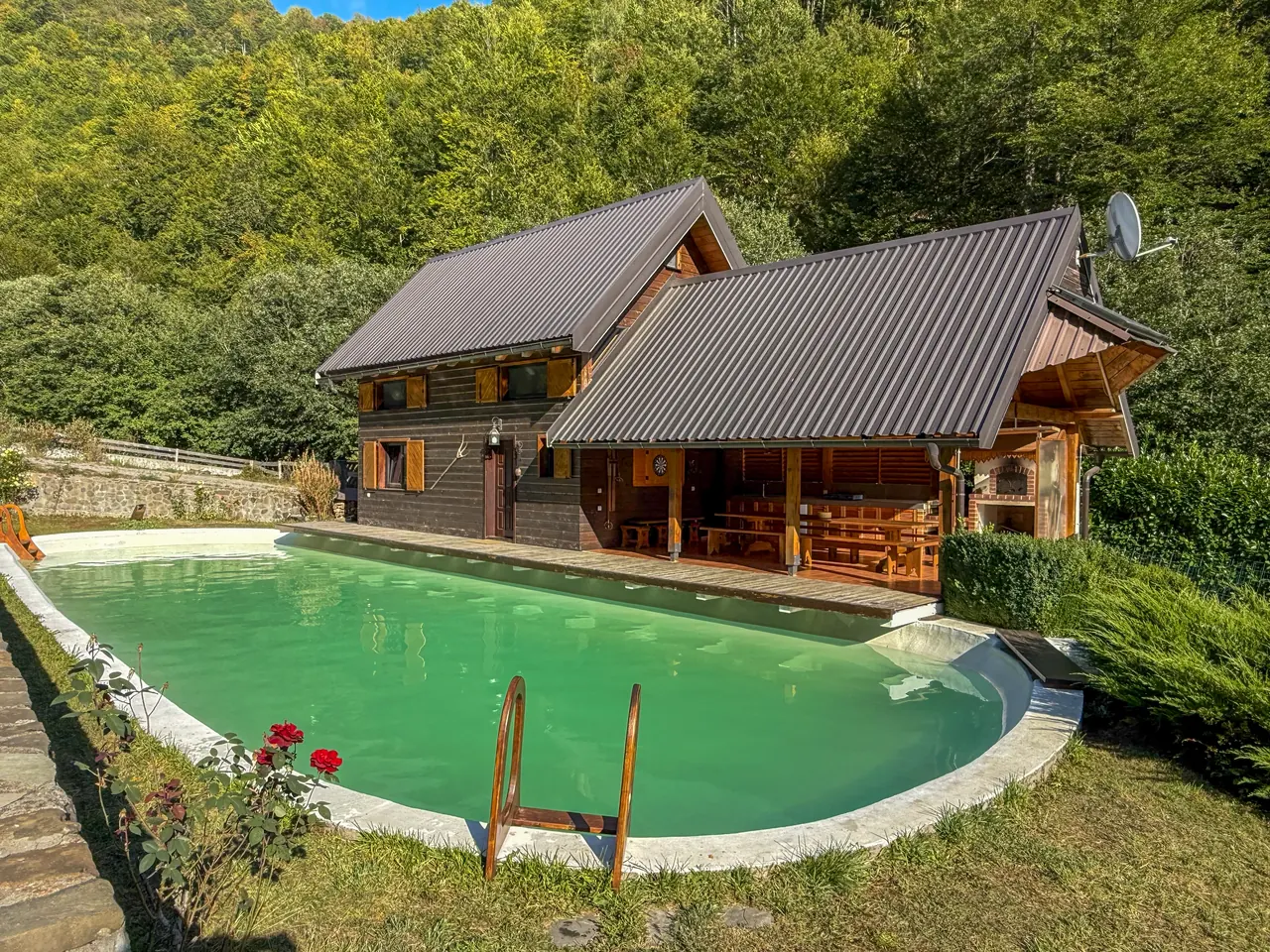 The wooden cabin and its long natural pool, seen from the lawn