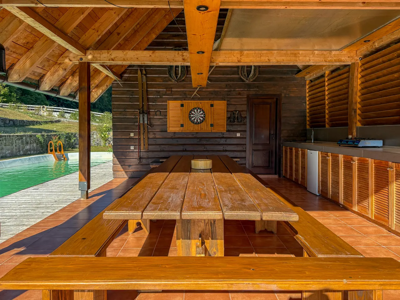 The long dining table under the covered terrace, with a dartboard