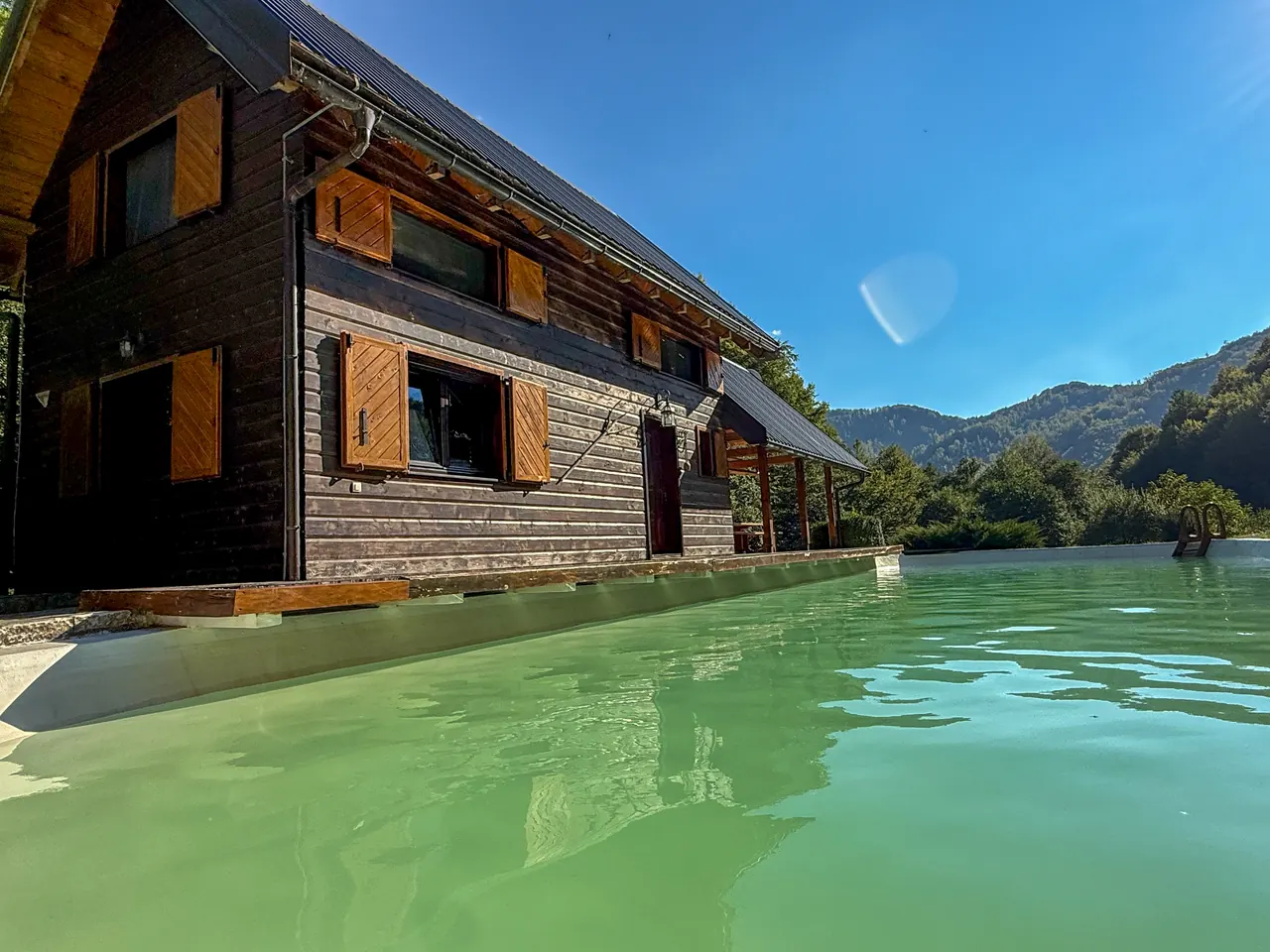 The dark timber cabin with orange shutters above the pool